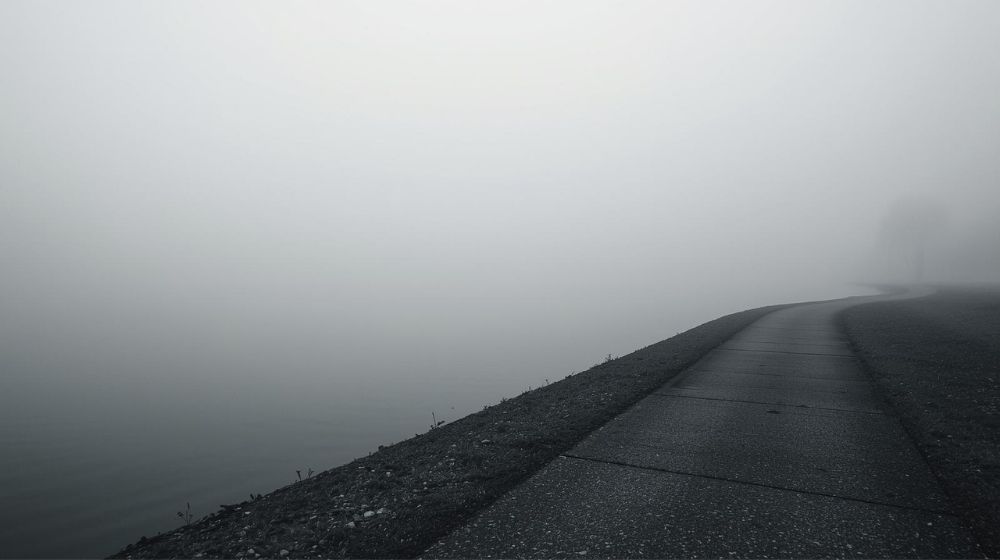 Fog-covered lakeside path fading into the distance, creating a quiet, contemplative scene.