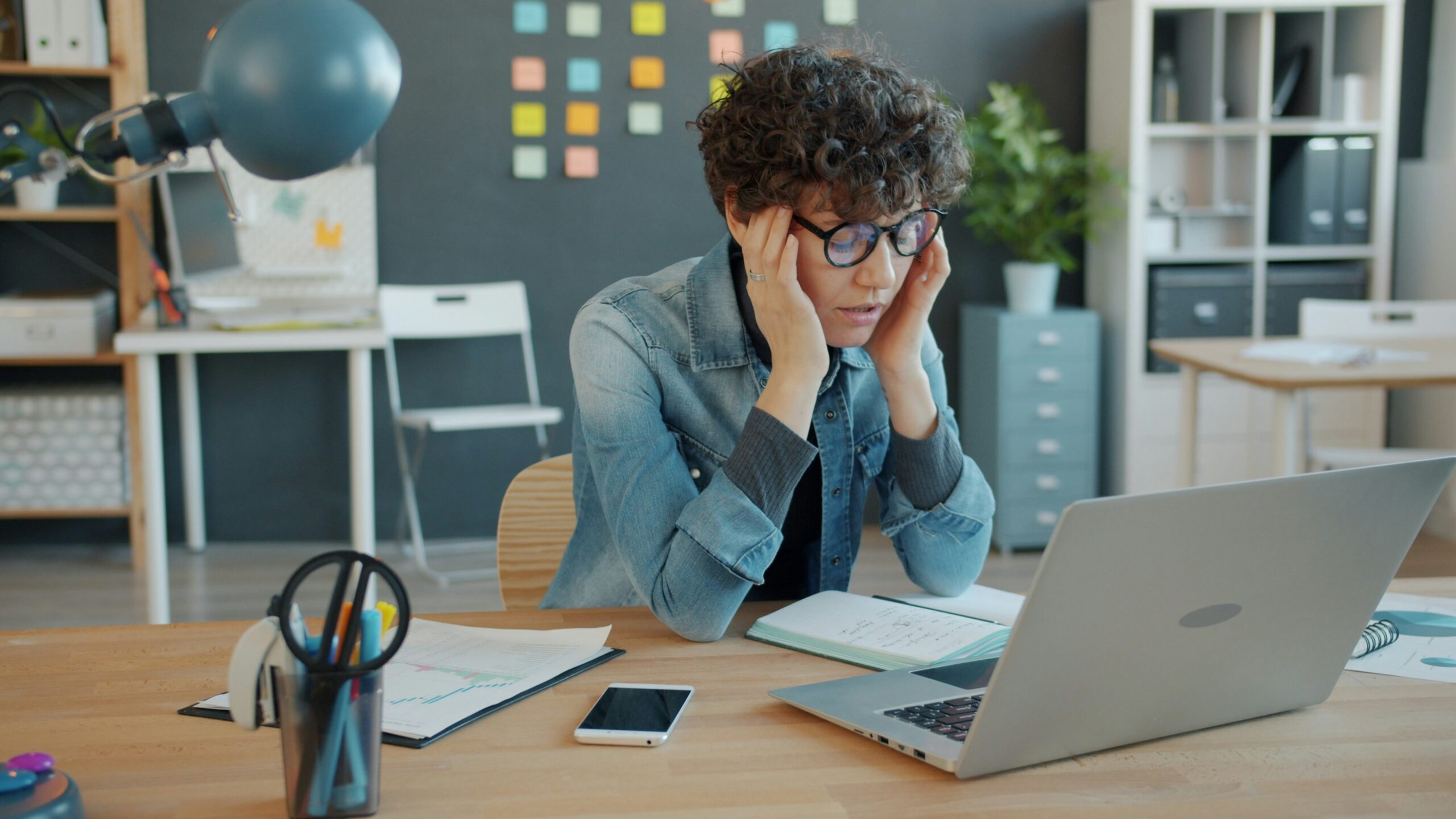 A tired woman sitting at a desk with her hands on her timples, feeling overwhelmed by work and emotional burnout—symbolizing the exhaustion that comes from overgiving.