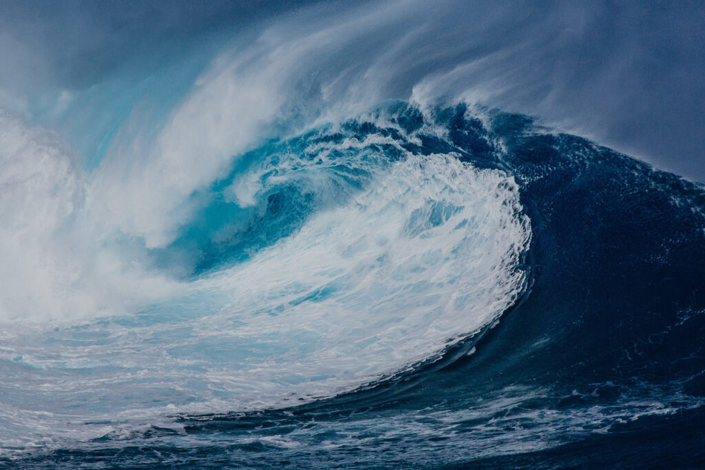 A powerful ocean wave curling forward, captured in motion with deep blue water and white spray.