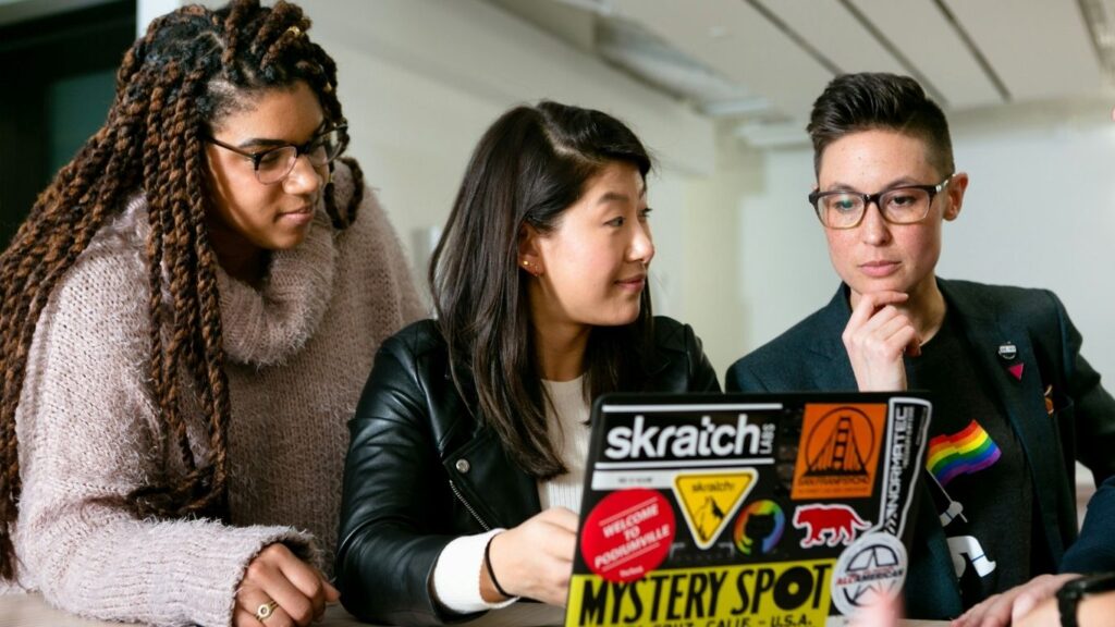 Three professionals collaborating at a laptop, reflecting thoughtful leadership, shared decision-making, and integrity in the workplace