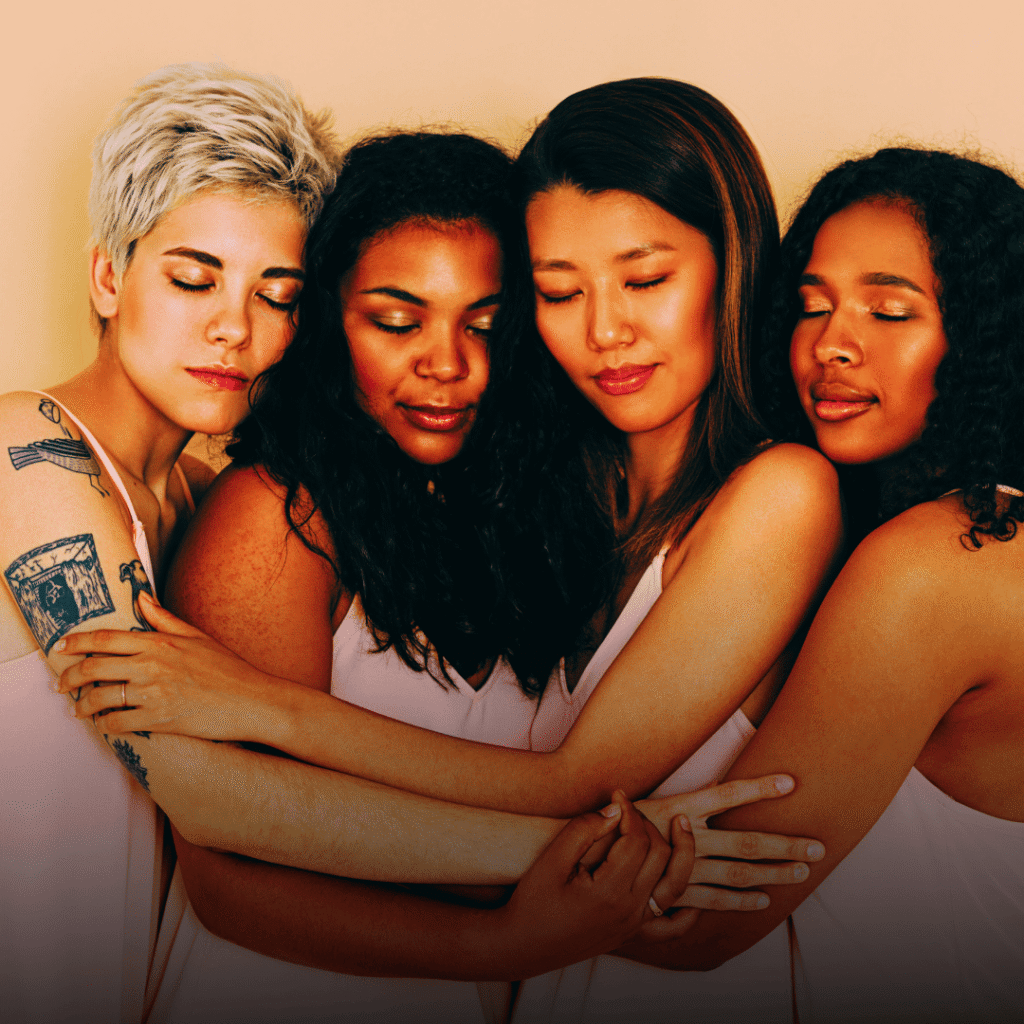 Four diverse women standing close together with their eyes closed, embracing one another in a moment of quiet unity and support. The image represents strong women learning to receive help, vulnerability, and connection instead of doing everything alone.